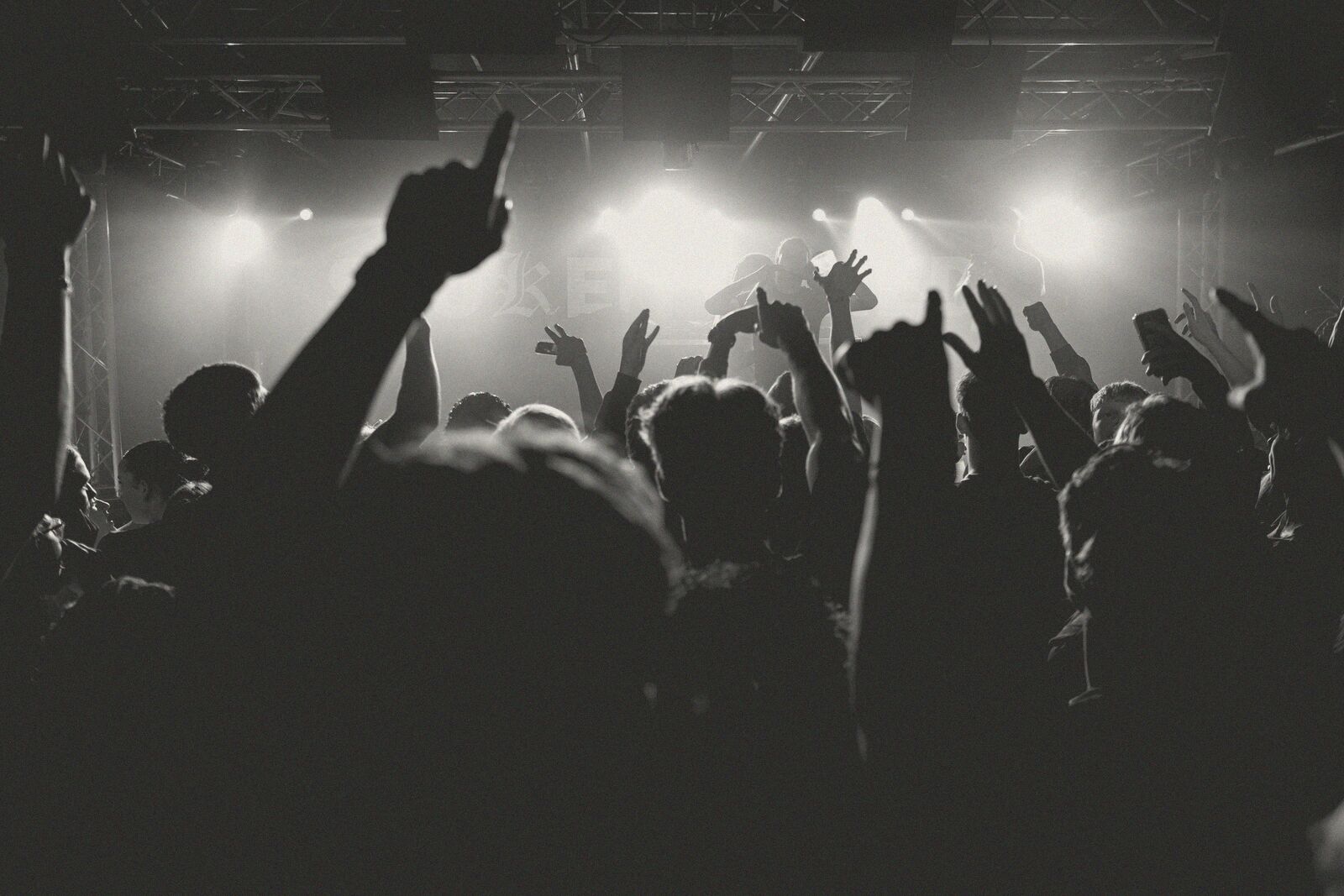 A crowd at a concert with their hands in the air under stage lights.