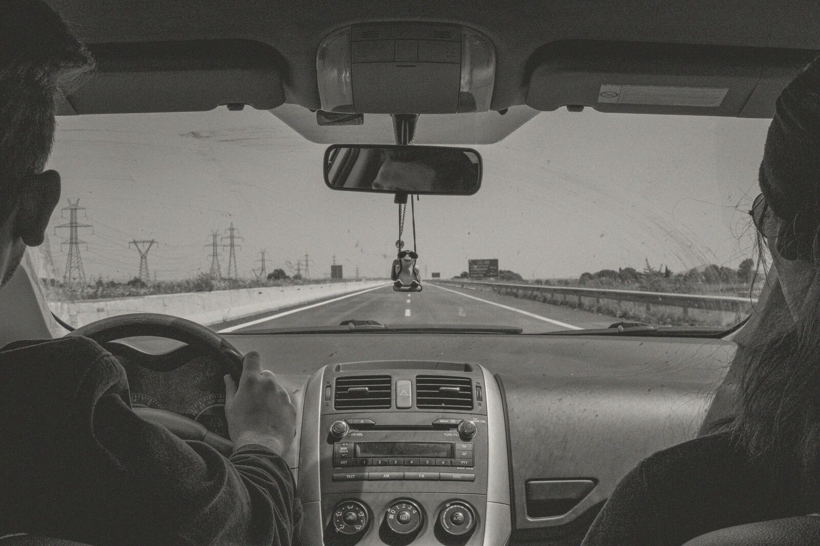 Two people in a car on an open road, seen from the back seat.